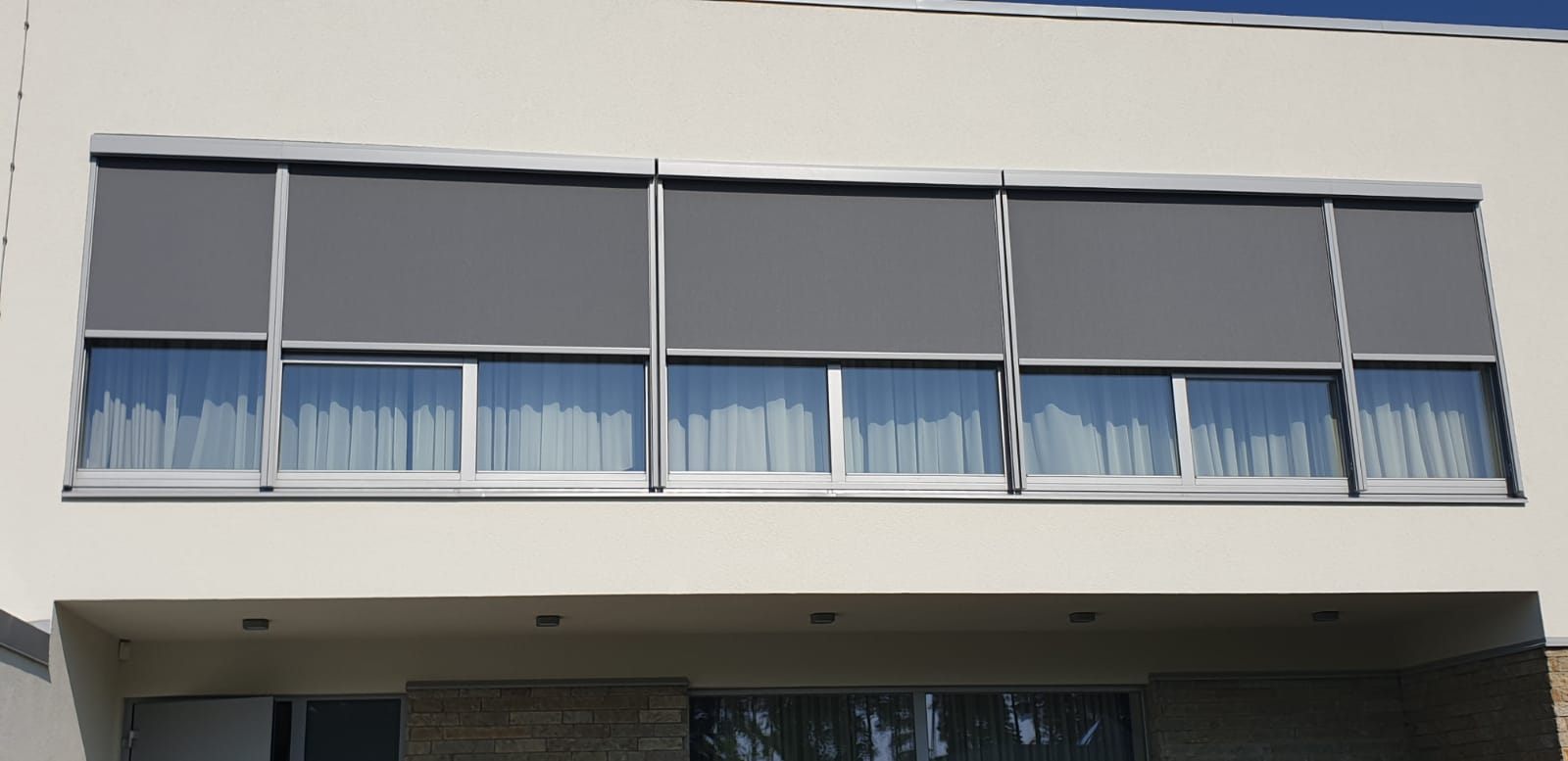 Graue Fassaden-Zip-Screens an einer langen Panoramaverglasung — FENSTORA, Riga