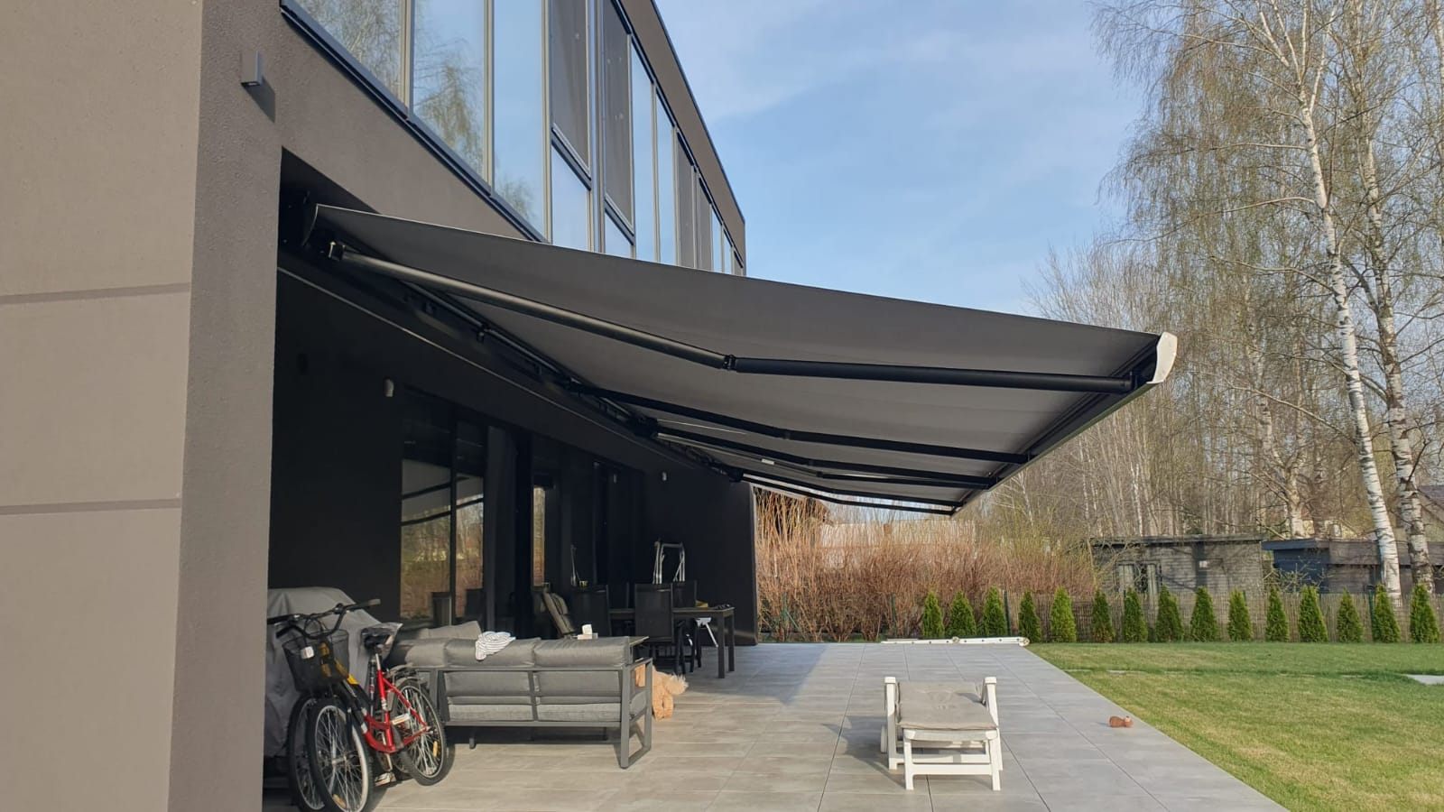 Antracīta izvelkama markīze pār modernas mājas terasi ar panorāmas stiklojumu — FENSTORA, Rīga
