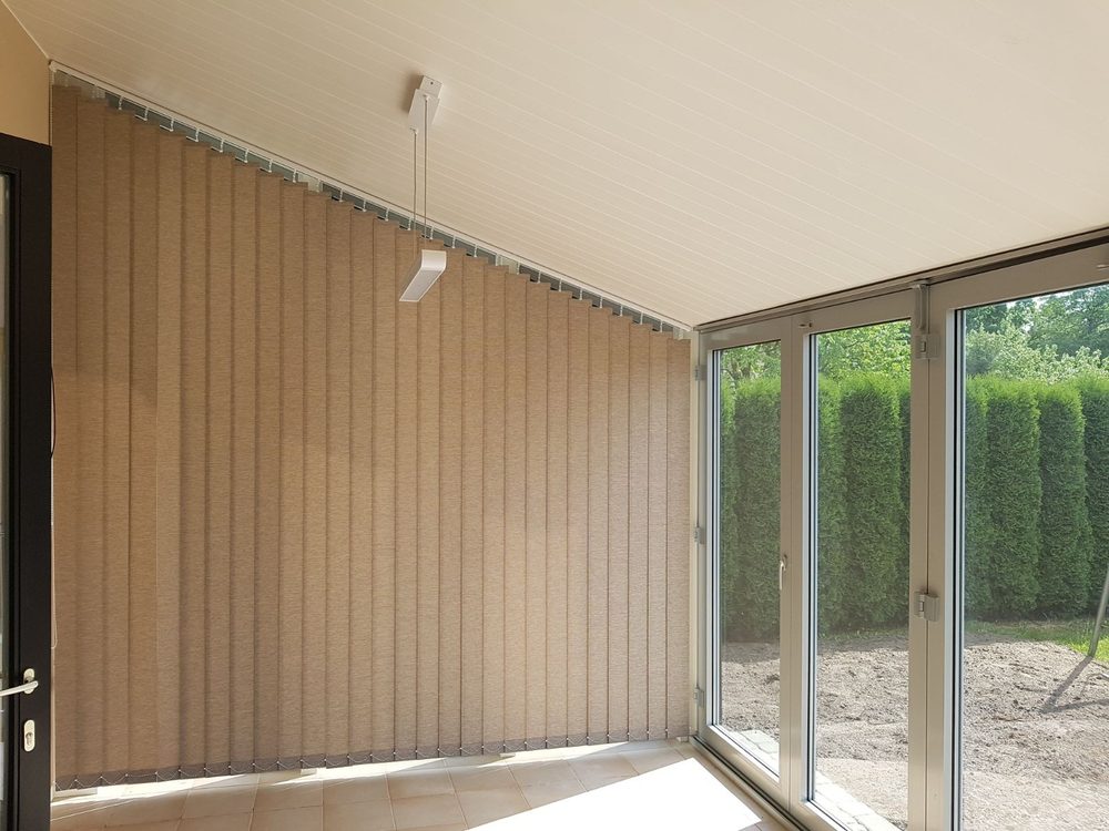 Brūnas vertikālās trapeces žalūzijas verandā ar slīpiem griestiem